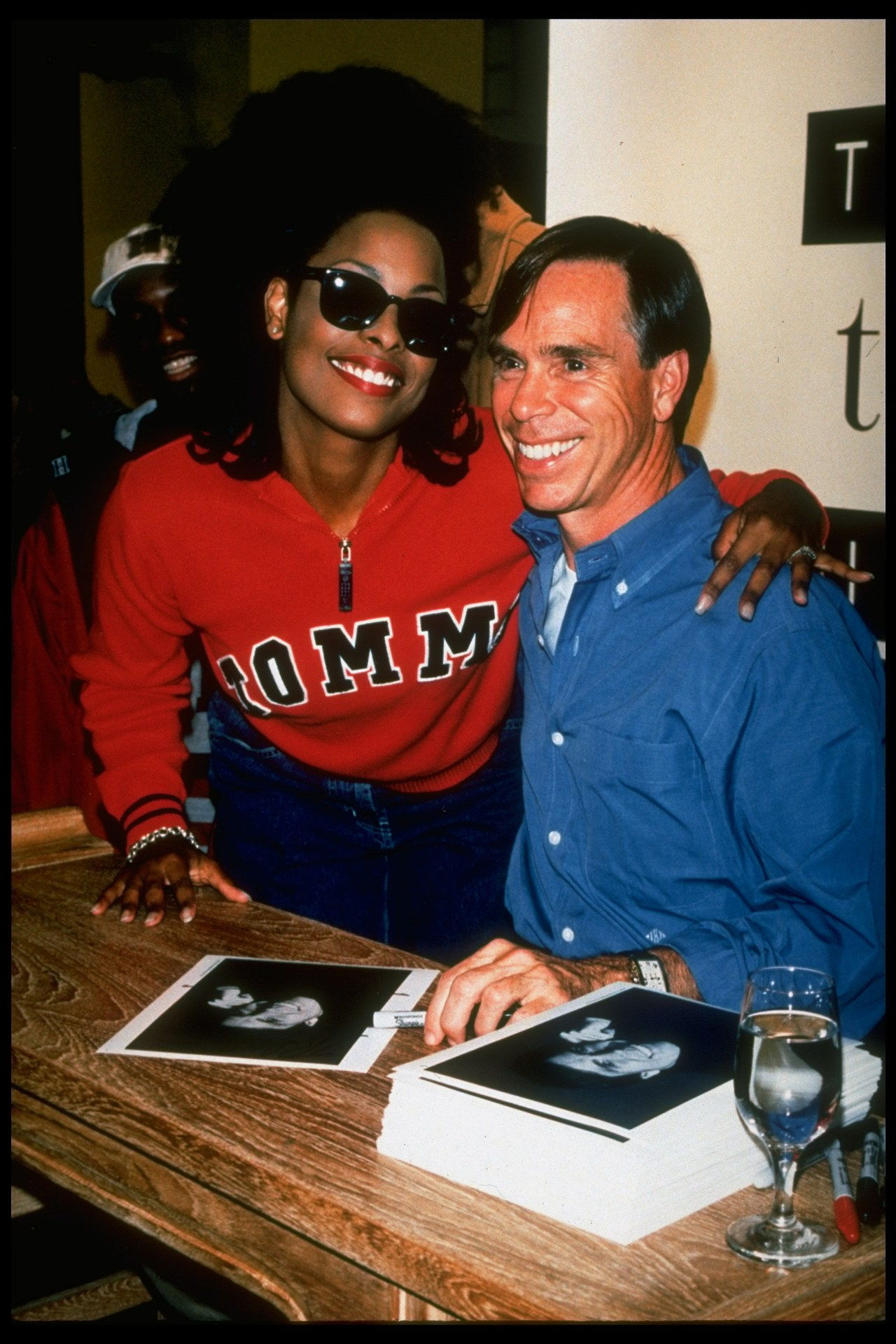 Moda designer Tommy Hilfiger (R) w. rap singer/model Spinerella w. stack of his publicity portraits at autograph party to launch his new women's clothing line called Tommy Girl, at Bloomingdale's dept. store. (Photo by James Keyser/The LIFE Images Collection/Getty Images)