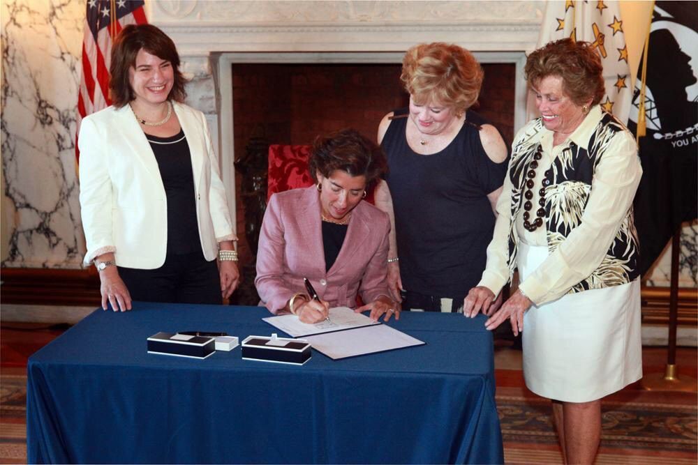 参议员 Gayle Goldin (left) attends a bill signing with Rhode Island Governor Gina Raimondo (center). 